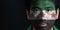 Portrait of a man with the flag of the Syrian Interim Government painted on his face on black background.