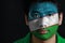 Portrait of a man with the flag of the Uzbekistan painted on his face on black background.