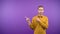 portrait of a man on an isolated purple background. man shows an arrow gesture with his fingers to the side. 4K