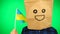 Portrait of man with paper bag on head waving Ukrainian flag with smiling face against green background.