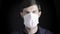 Portrait of a man putting on a medical mask on a black background, studio shot. The concept of prevention of viral and