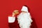 Portrait of man in santa costume standing on red background with burger in hand, hungry looking aside for fast food. Santa will