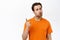 Portrait of man shaking finger in disapproval, scolding someone, threating, standing in orange tshirt over white