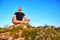 Portrait of the man sitting on a rock in the lotus position against blue sky.