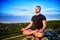 Portrait of the man sitting on a rock in the lotus position against blue sky.