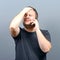 Portrait of a man slapping his forehead while talking on cellphone against gray background