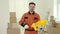 Portrait of the man worker standing, holding paint roller and plastic tub in new apartment renovation room. Craftsman in