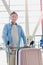 Portrait of mature attractive man pushing cart with his suitcase for check in at airport