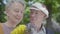 Portrait of a mature couple in love sitting on a bench in the park. Adult woman and her elderly husband sniffing a