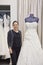 Portrait of a mature employee standing by elegant wedding dress in bridal store