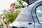 Portrait of mature female gardener putting flowers on car trunk for delivery