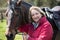 Portrait Of Mature Female Owner In Field With Horse