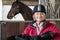 Portrait Of Mature Female Owner Holding Saddle In Stable With Ho