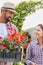 Portrait of mature gardener carrying flowers on crate for the female customer in shop