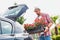 Portrait of mature gardener putting flowers on crate in car trunk for delivery