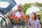 Portrait of mature gardener putting flowers on crate in car trunk while talking to woman in garden shop