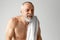 Portrait of mature, grey-haired, shirtless man doing morning routine, washing face, taking care after skin against grey