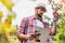 Portrait of mature man examining plants growing in garden while writing report on clipboard