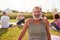 Portrait Of Mature Man On Outdoor Yoga Retreat With Friends And Campsite In Background