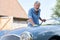 Portrait Of Mature Man Polishing Restored Classic Sports Car Outdoors At Home