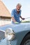 Portrait Of Mature Man Polishing Restored Classic Sports Car Outdoors At Home