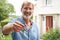 Portrait Of Mature Man Standing In Garden In Front Of Dream Home In Countryside Holding Keys