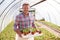 Portrait Of Mature Man Working In Garden Center Greenhouse Holding Tray Of Seedlings In Pots