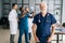 Portrait of mature older surgeon wearing blue uniform standing in medical meeting office, looking at camera.