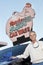 Portrait of mature owner of car wash standing below signboard with vehicle