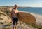 Portrait of mature senior Surfer looking at the ocean with vintage surfboard on an empty beach