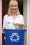 Portrait Of Mature Woman Holding Recycling Bin Of Reusable Waste Outside Front Door