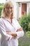 Portrait Of Mature Woman Standing In Garden In Front Of Dream Home In Countryside