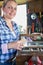 Portrait Of Mature Woman Upcycling Furniture In Workshop At Home Rubbing Down Cabinet With Sandpaper