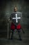 Portrait of medieval warrior, dark skinned bald knight with dirty wounded face holding shield and sword isolated over
