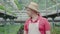 Portrait of mid-adult Caucasian man in straw hat looking around in greenhouse and smiling. Positive male worker standing