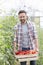 Portrait of mid adult farmer carrying tomatoes in crate at farm