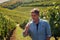 Portrait of middle age winemaker sommelier holding glass, smelling and tasting wine in vineyard