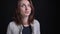 Portrait of middle-aged brunette caucasian woman watching thoughtfully into camera on black background.