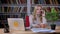 Portrait of middle-aged caucasian blonde talking on cellphone and making notes in office on bookshelves background.