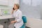 Portrait of middle-aged female medical practitioner sitting at desk with laptop , explain recommendation, discuss