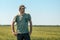 Portrait of middle-aged male farm worker posing in green t-shirt and trucker hat, standing in unripe barley crop field on bright