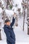 Portrait of middle-aged man having fun while shaking snow from tree branches in winter forest after snowfall. Winter holidays,