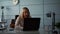 A portrait of a middle-aged woman with blond hair, sitting in an office with a laptop on a chair, talking and laughing