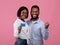 Portrait of millennial black couple with credit card gesturing YES, recommending bank services on pink studio background