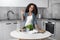 Portrait of mixed-race curly teen girl standing in the kitchen in front of a table with vegetables and a book for