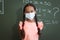 Portrait of mixed race schoolgirl in face mask standing in front of chalkboard in maths classroom