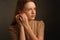 Portrait of a model brown-haired in a white dress on a dark background in the Studio. fastens the earring, hands at the ear