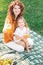 Portrait of mommy and her kid showing plastic cups with orange juice sitting on the blanket in the park