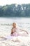 Portrait of a mother blonde and her daughter in beautiful dresses on the sand with a lake on the background. Happy family enjoying