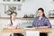 Portrait of mother with her adolescent daughter sitting at table in kitchen, looking at camera